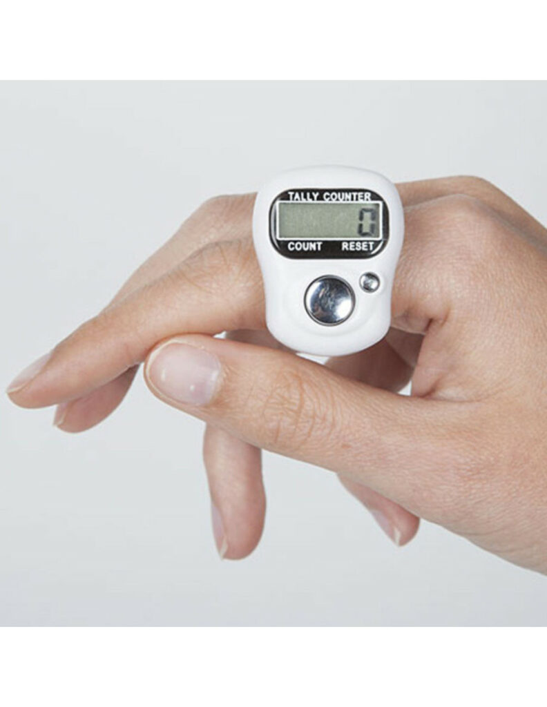 Bague compte-rangs numérique noire avec écran LCD, portée sur un index pour compter les rangs d'un tricot.