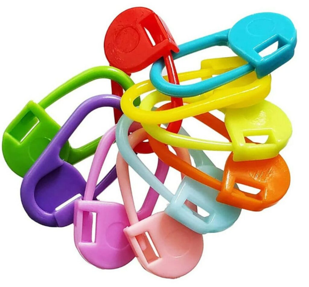 Lot de 10 marqueurs de maille de différentes couleurs vives (bleu, vert, rose), certains de type anneau et d'autres de type épingle, posés sur une table en bois à côté d'une pelote de laine.