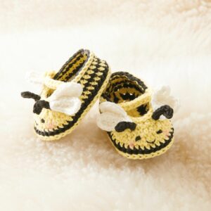 Kit crochet Ricorumi Abeille présentant des chaussons pour bébé rayés sur une couverture douce, décoration de naissance solaire et artisanale.
