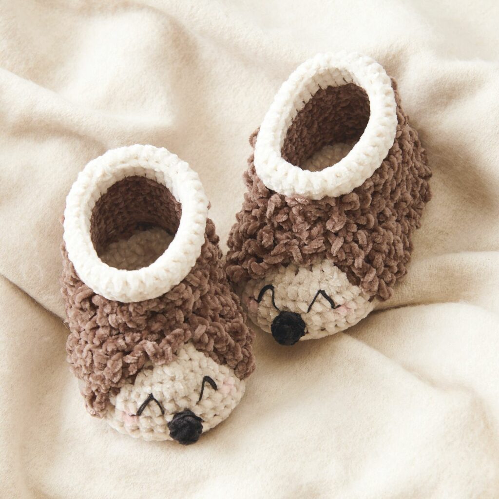 Kit crochet Ricorumi pour chaussons hérisson présentés sur une couverture douce, mise en scène de naissance chaleureuse et lumineuse