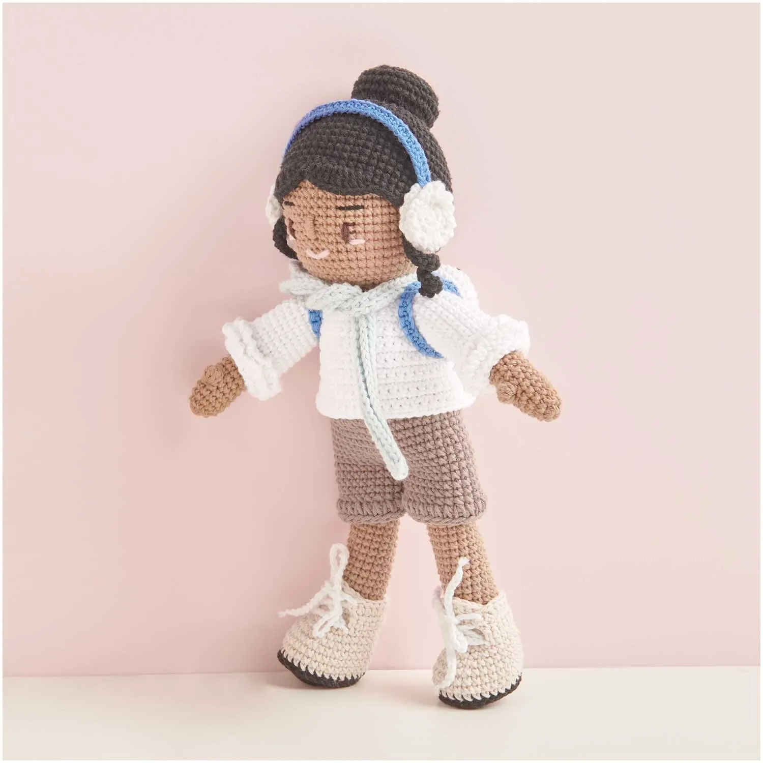 Poupée amigurumi en tenue d'hiver avec cache-oreilles et petit sac à dos, réalisée avec les pelotes de coton Ricorumi.
